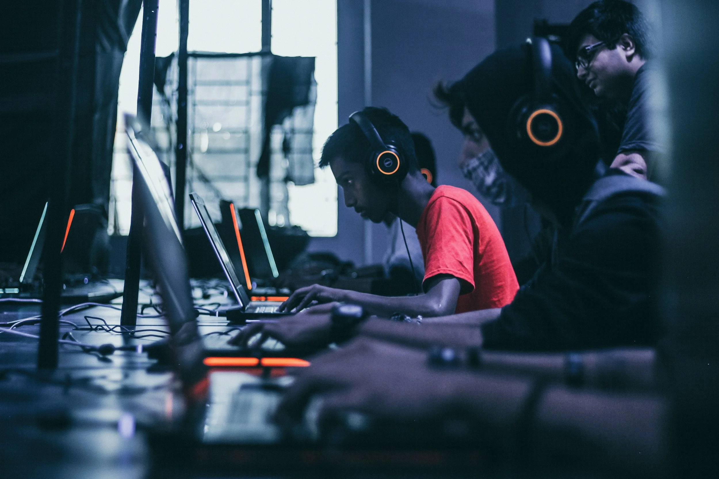 Group of young people working on computers in a dimly lit room with headphones on.